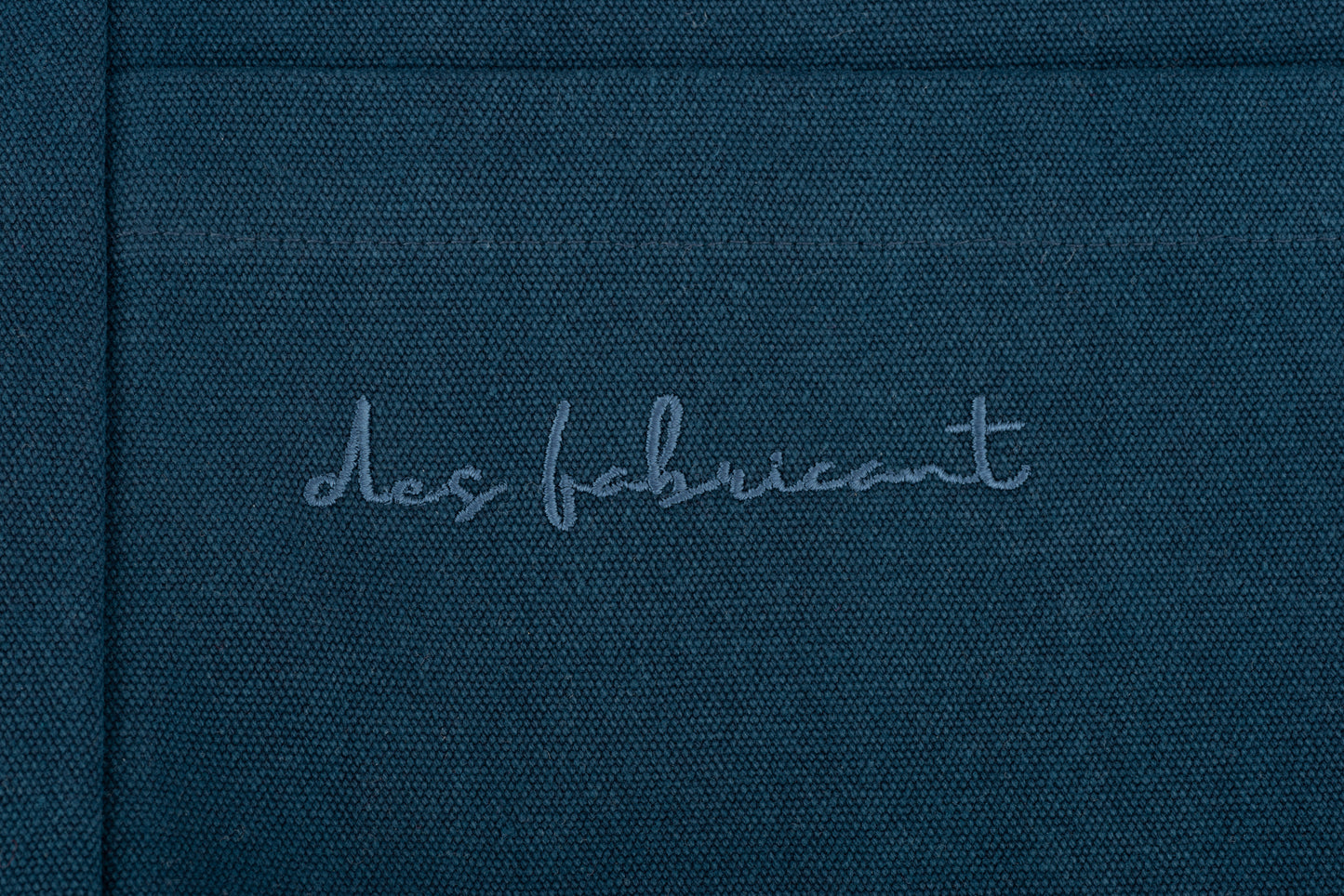 Embossed Des Fabricant logo detail on premium dark blue cotton fabric -subtle, refined branding.