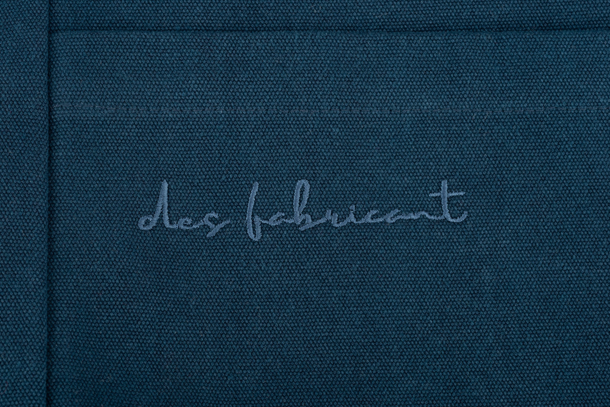 Embossed Des Fabricant logo detail on premium dark blue cotton fabric -subtle, refined branding.